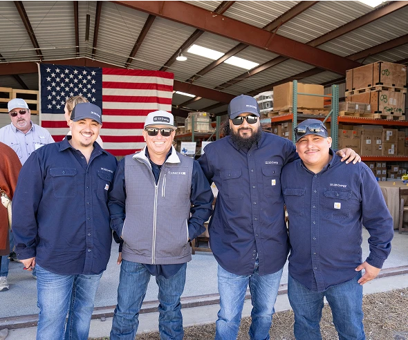 Four SB Energy workers wearing blue shirts standing in front of an American flag inside a warehouse.