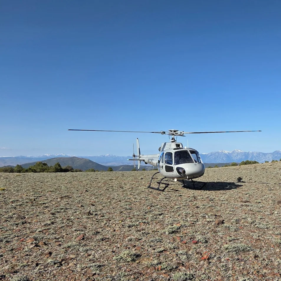 A helicopter on a rocky terrain with a clear blue sky and mountains in the background.
